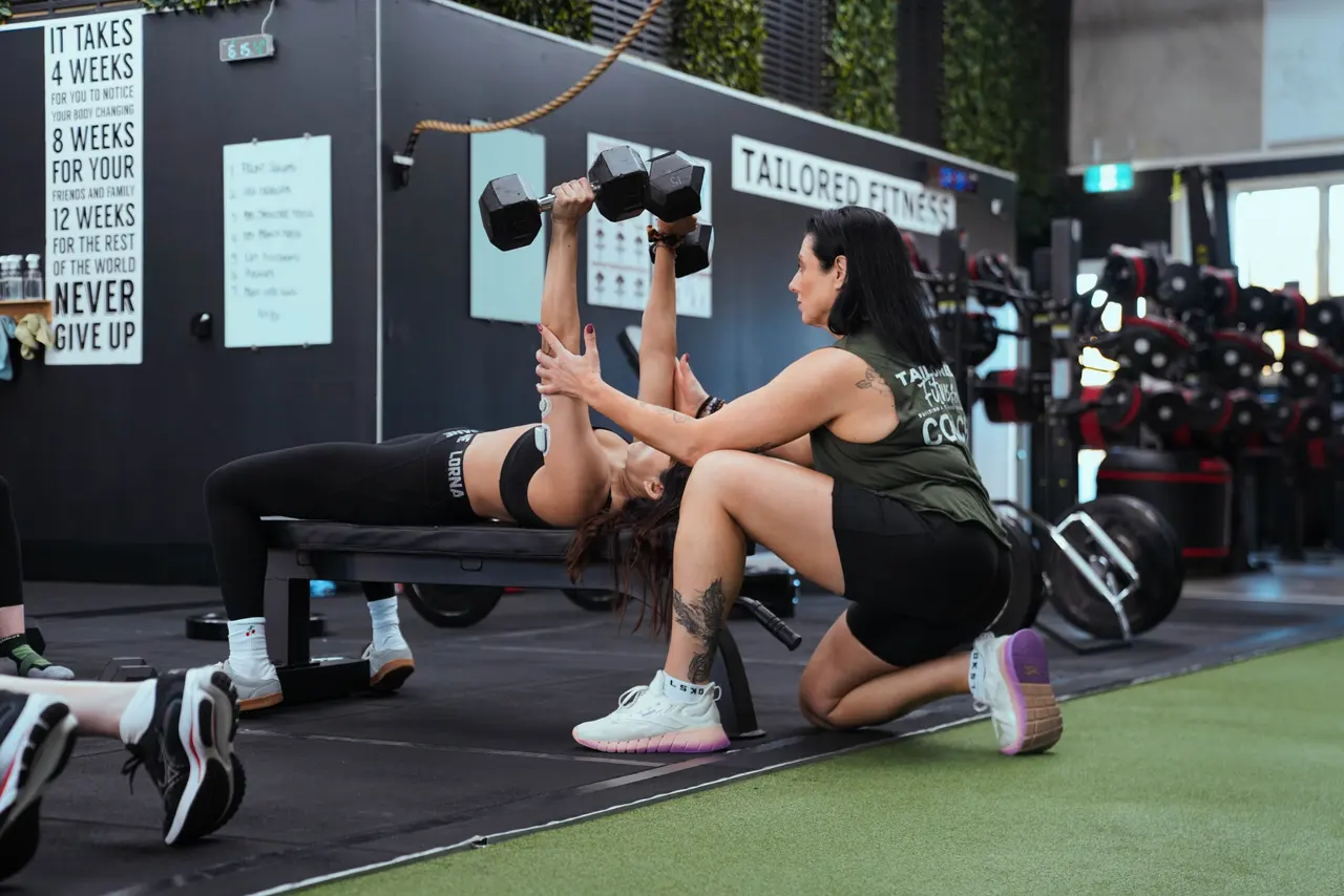 A coach working one-to-one with a member through a dumbbell press