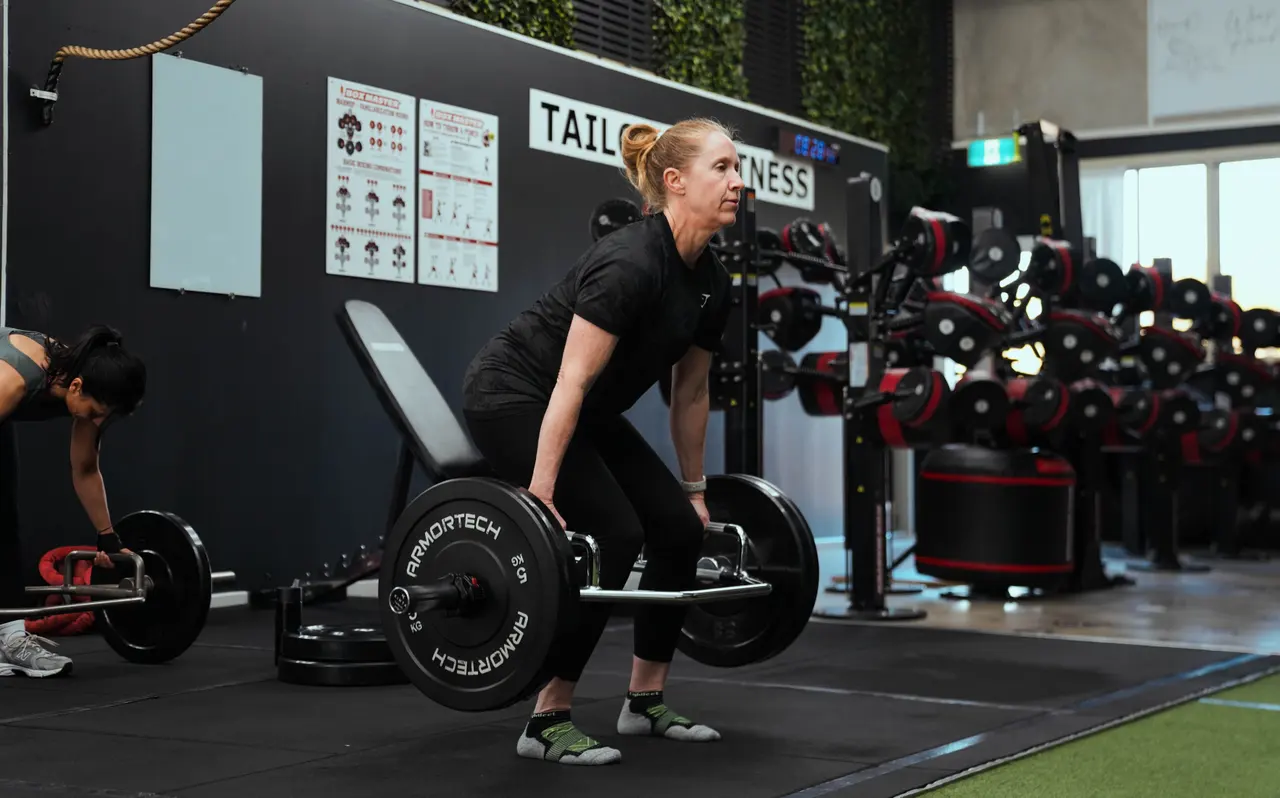 Coach and member mid trap-bar deadlift, studio signage behind