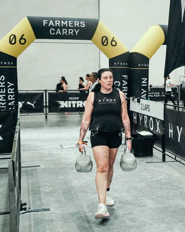 A competitor finishing the farmers carry under the HYROX arch